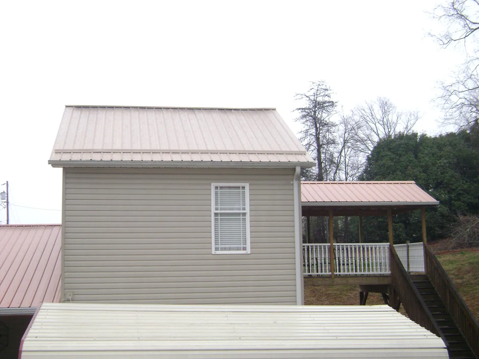 Tan metal roofs on a two story addition and attached porch, from a Roof Replacement job in Smithfield